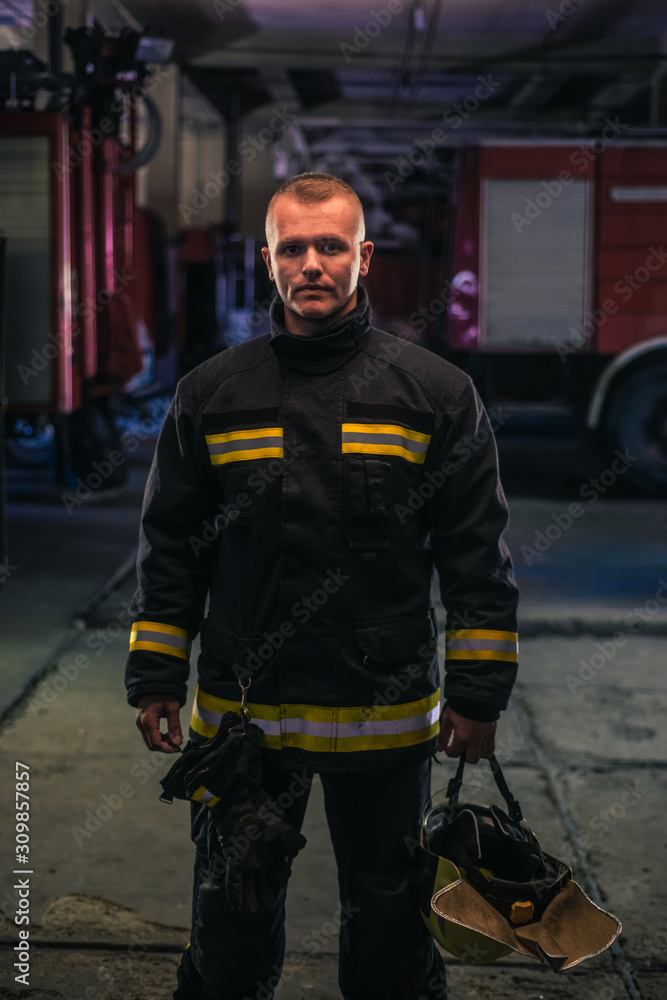 Fototapeta premium Portrait of young fireman standing inside the fire station.
