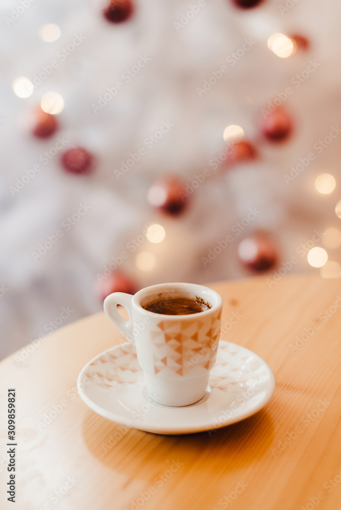 Cup of espresso or short coffee in white cup in cosy Christmas arrangement, festive decoration with white bokeh background, copy space
