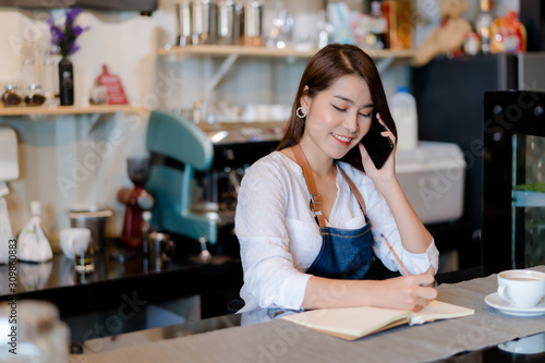 Asian woman Barista calling with customer at front counter occupation, part-time,job or owner business working woman happy selling and making drink beverage