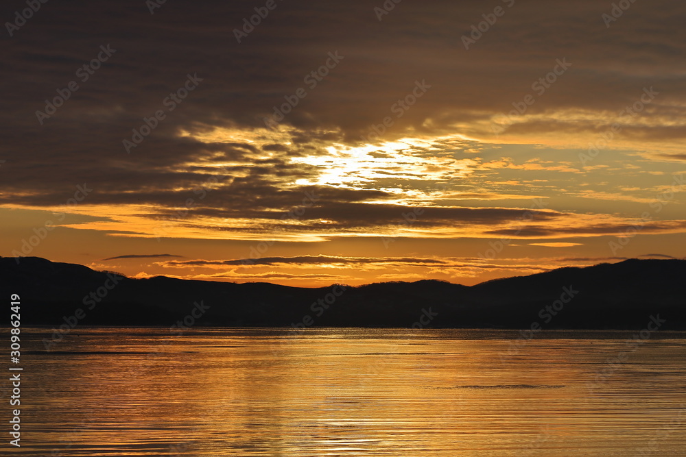 Naklejka premium Sunrise in partly cloudy morning over the calm sea. Dawn near the shore of the Sea of Japan.