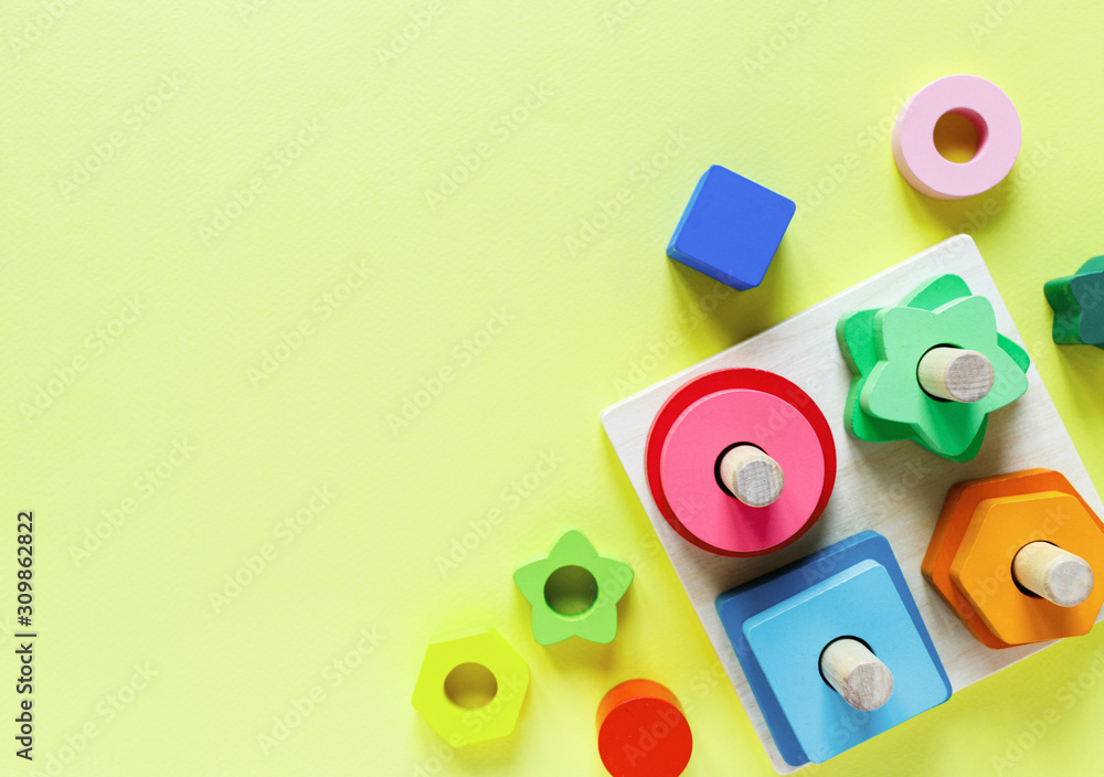 Fototapeta premium Wooden kids toys on colourful paper. Educational toys blocks. Toys for kindergarten, preschool or daycare. Copy space for text. Top view