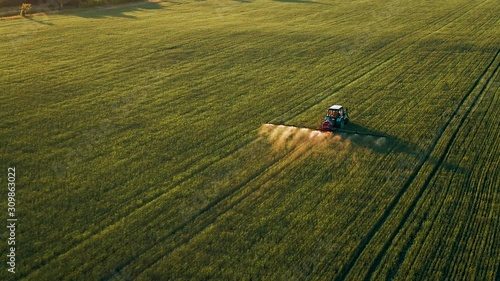 Farm tractor spraying plants in the field. Russia Pskov region. Sun rays on horizon