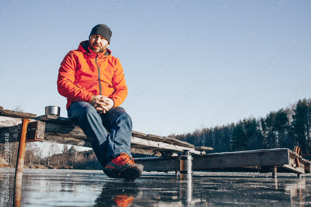 A lone tramp traveler stands on ice and drinks tea from a thermos. A lone tramp traveler stands on ice and drinks tea from a thermos.
