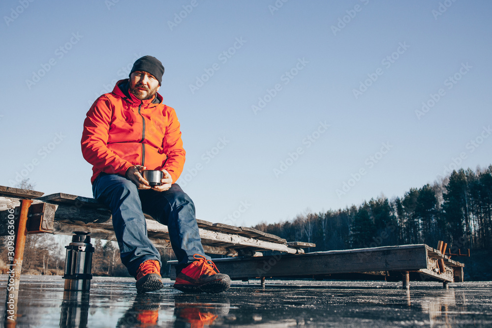 A lone tramp traveler stands on ice and drinks tea from a thermos. A lone tramp traveler stands on ice and drinks tea from a thermos.