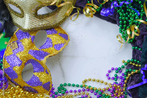 Mardis Gras border on marble background includes harlequin mask with green, gold and purple beads and matching fabrics. Copy space photo