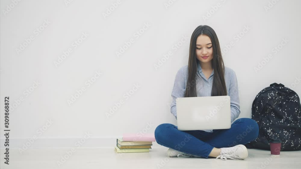 Young asian lady sitting on the floor in lotos position, searching something in her laptop, taking apple out from her bag, puttingit on the stack of books. Young asian lady sitting on the floor in lotos position, searching something in her laptop, taking apple out from her bag, puttingit on the stack of books.