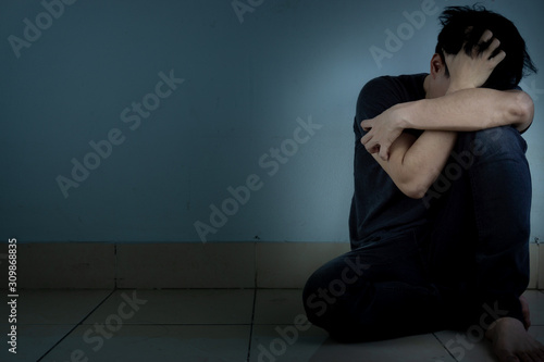 sad man hug his knee and cry sitting alone in a dark room. Depression, unhappy, stressed and anxiety disorder concept © saran