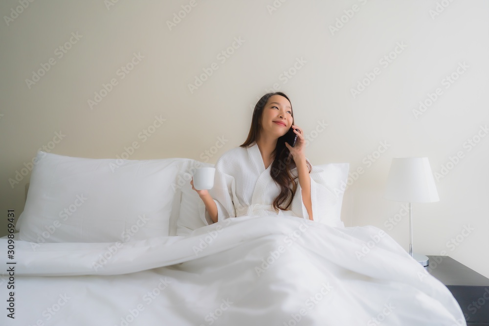 © siraphol - Portrait beautiful young asian women with coffee cup and mobile phone on bed © siraphol - Portrait beautiful young asian women with coffee cup and mobile phone on bed