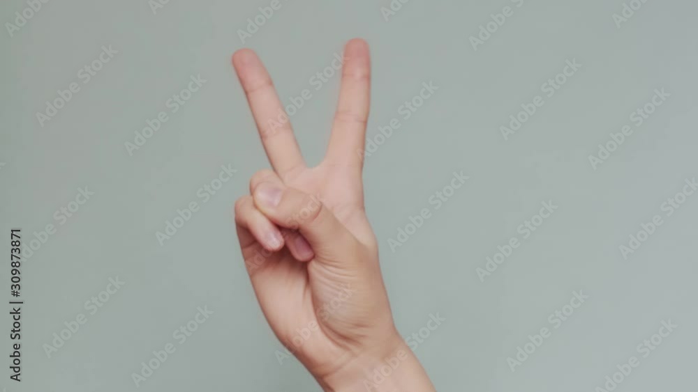 Female hand holding peace gesture on copy space blue background close up. Faceless woman showing victory sign isolated on grey mock up screen. Happiness optimism friendship language Female hand holding peace gesture on copy space blue background close up. Faceless woman showing victory sign isolated on grey mock up screen. Happiness optimism friendship language