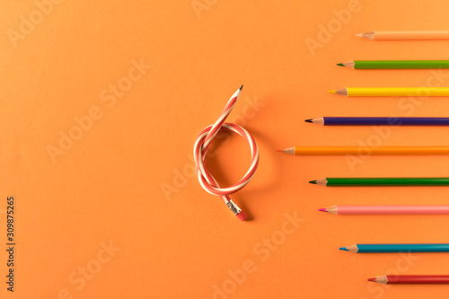 Colored pencils with one flexible pencil on orange background. The concept of flexibility in decision-making.