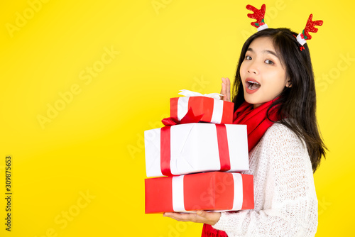 Happy Asian teenager girl holding gift boxes on yellow background.