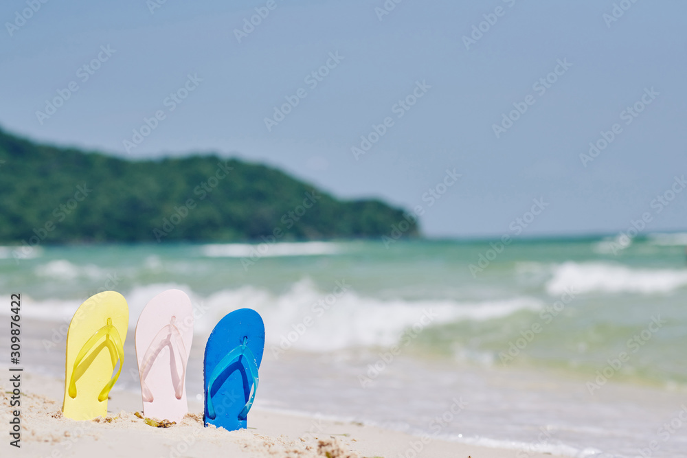 Three flip-flops on the sunny tropical beach, sea waves in background