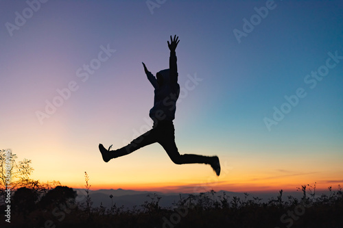 Silhouette of happy people jumping playing on mountain at sunset