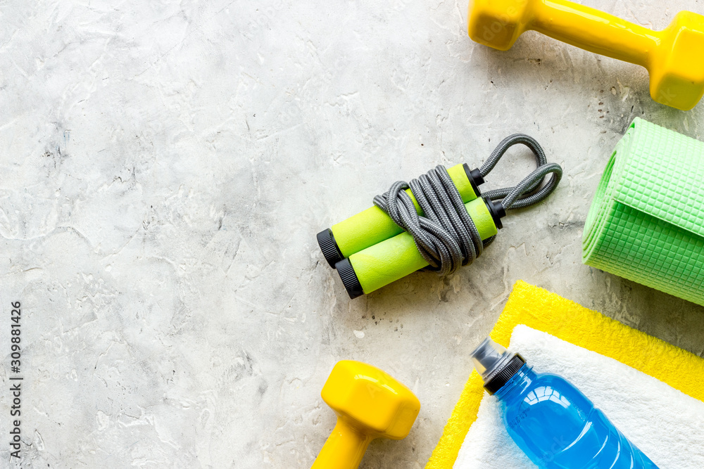 Gym equipment - dumbbells, jump rope - frame on grey background top-down copy space