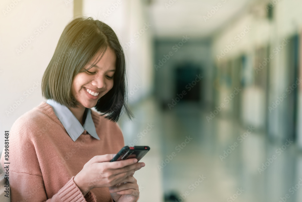 A smiling Asian female high school student is sitting and enjoying social media on her smartphone in the school. A smiling Asian female high school student is sitting and enjoying social media on her smartphone in the school.
