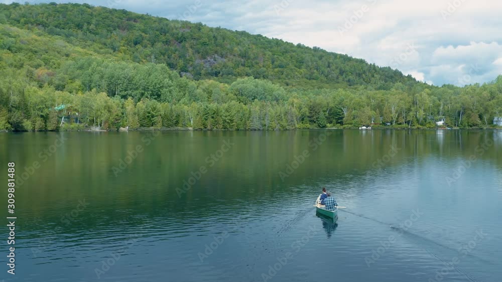 Aerial: Father and daughter paddling and fishing in a canoe on a calm blue lake. Quebec, Canada. Aerial: Father and daughter paddling and fishing in a canoe on a calm blue lake. Quebec, Canada.