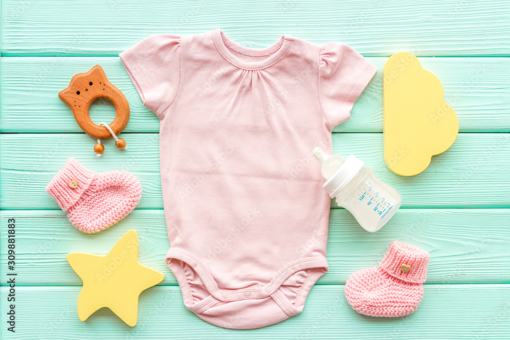 Pink bodysuit for baby girl near children's things on green wooden background top-down Pink bodysuit for baby girl near children's things on green wooden background top-down