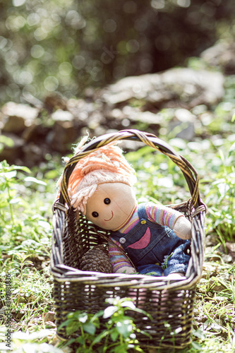 Cute girl toy doll on a basket on a green grass ground cute forest portrait photo