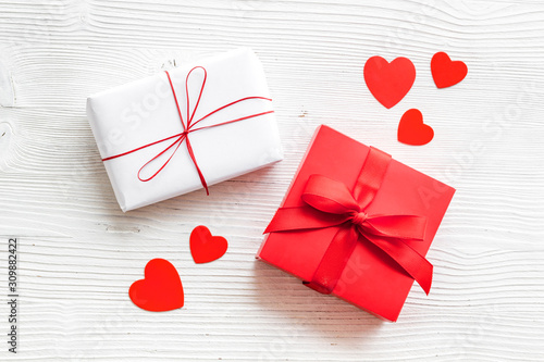 Present to a lover on Valentine's Day. Gift boxes near paper hearts on white wooden background top-down.