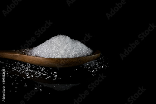 sugar in wooden spoon on dark background