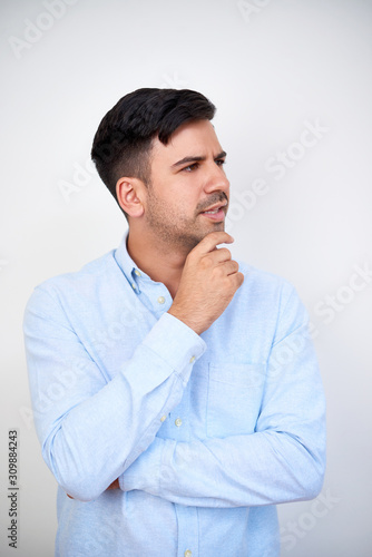 Portrait of pensive young businessman in light blue shirt touching chin and looking away