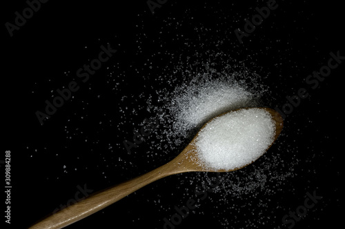 sugar in wooden spoon on black background