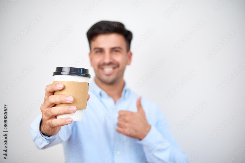 Positive young Caucasian entrepreneur showing thumbs-up and giving cup of take away coffee Positive young Caucasian entrepreneur showing thumbs-up and giving cup of take away coffee