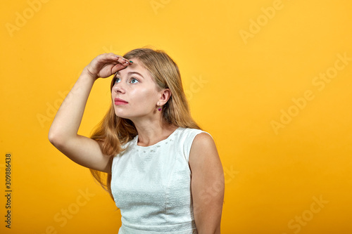 Disappointed caucasian young lady keeping hand on forehead, looking into distance over isolated orange background wearing white shirt. Lifestyle concept