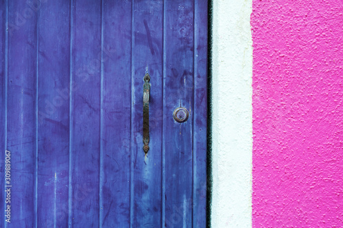 Wooden violet door and pink wall. Close up view. Colorful architecture in Burano island, Venice, Italy.