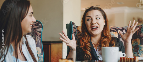 Beautiful young plus size women story telling to her girlfriend while drinking coffee in coffee shop. photo