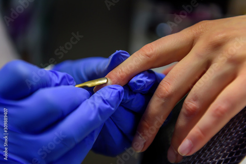 Cuticle removal  close-up. Manicure in the salon. Manicurist in blue gloves shifts the cuticle of the nail with metal spatula.