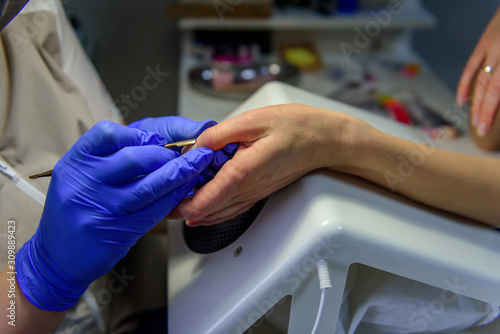 Cuticle removal, close-up. Manicure in the salon. Manicurist in blue gloves shifts the cuticle of the nail with metal spatula.