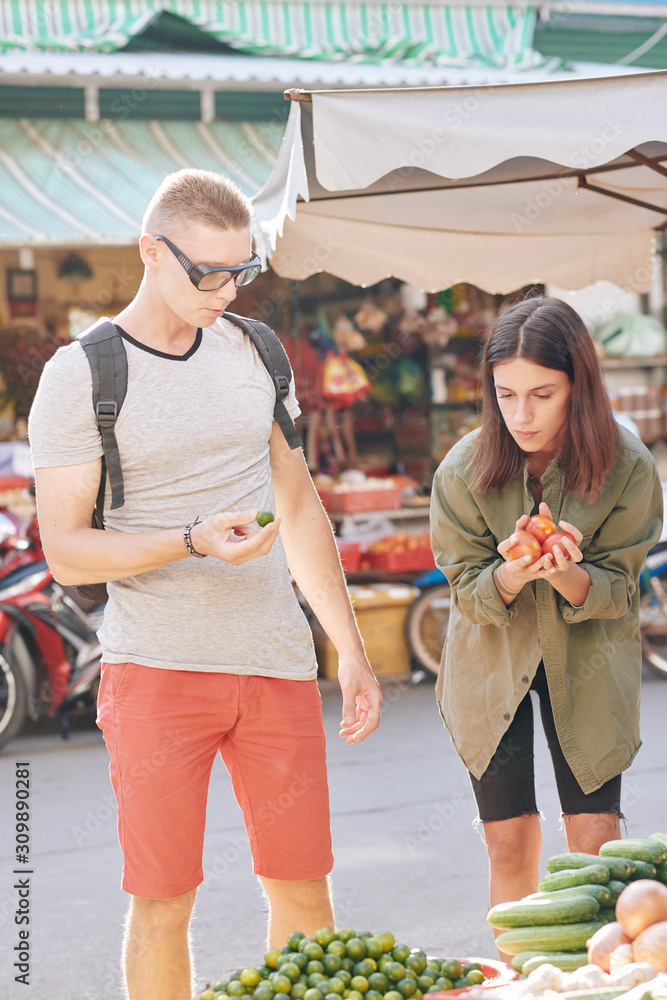 Young Caucasian couple buying fresh local fruits and vegetables at street market