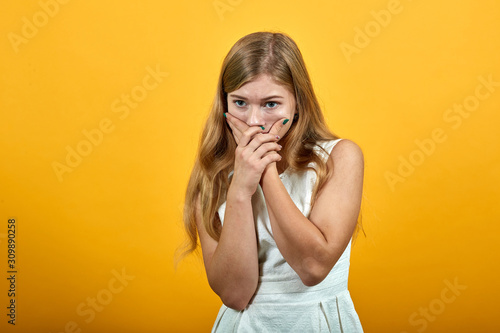 Scared young woman in fashion white shirt over isolated orange background, covering mouth with hands, looking frightened. Lifestyle concept