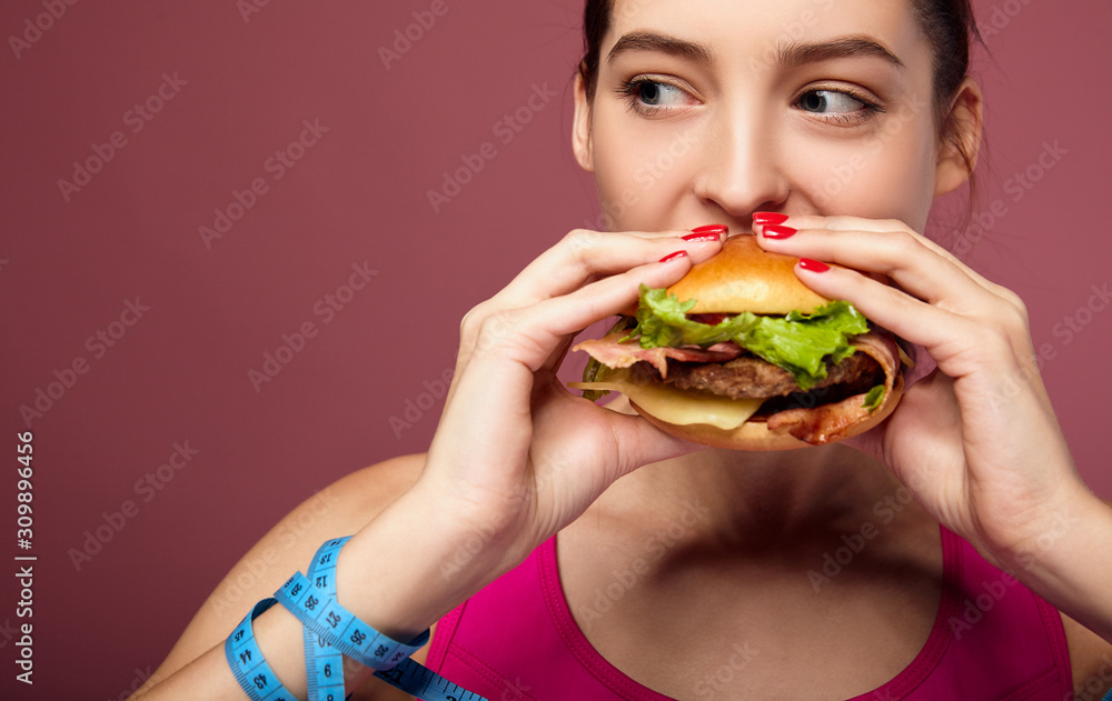 Lovely diet girl enjoys eating a big cheeseburger with pleasure. Lovely diet girl enjoys eating a big cheeseburger with pleasure.