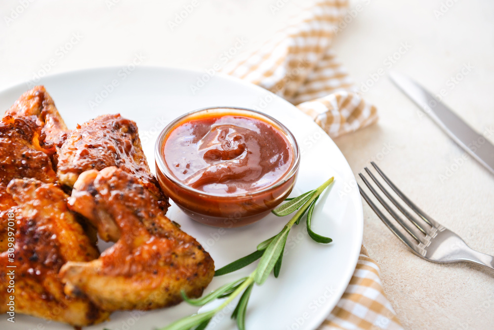 Plate with tasty fried chicken wings and barbecue sauce on white table Plate with tasty fried chicken wings and barbecue sauce on white table