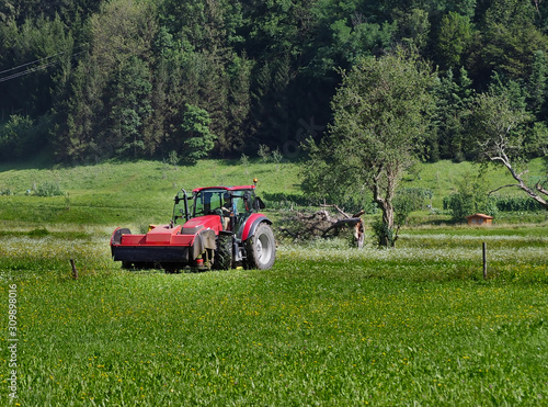 Tractor with front rotary mower machine in a field on the sidelines of the forest.