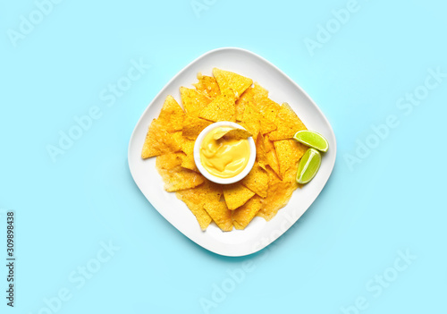 Plate with tasty nachos and sauce on color background