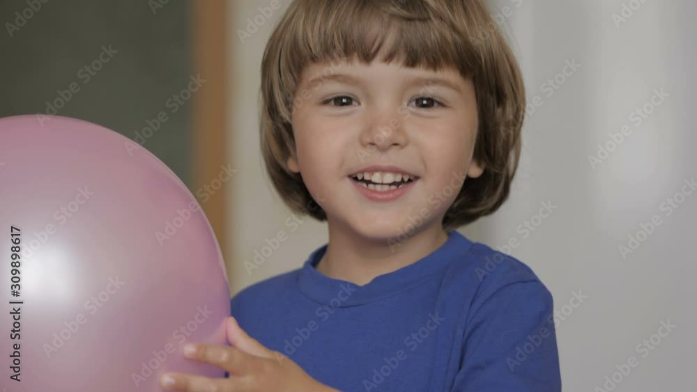 Little Boy Looks Out From Behind Balloon and Laughs Happily. Close up Portrait of a Happy Little Child Bursting in Laugh. Child Boy Blonde With Blue Eyes and Laughs Indoors. Closeup. Slow Motion. Little Boy Looks Out From Behind Balloon and Laughs Happily. Close up Portrait of a Happy Little Child Bursting in Laugh. Child Boy Blonde With Blue Eyes and Laughs Indoors. Closeup. Slow Motion.
