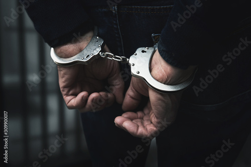 Obraz na plátně arrested man with cuffed hands behind prison bars