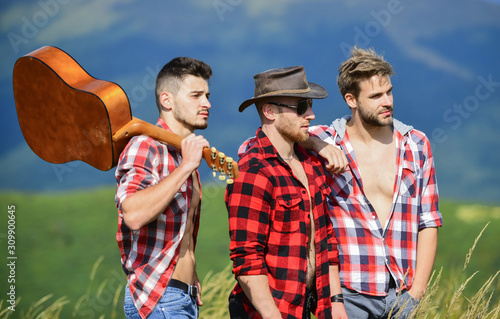 Long route. Adventurers squad. Men with guitar hiking on sunny day. Group of young people in checkered shirts walking together on top of mountain. Tourists hiking concept. Hiking with friends