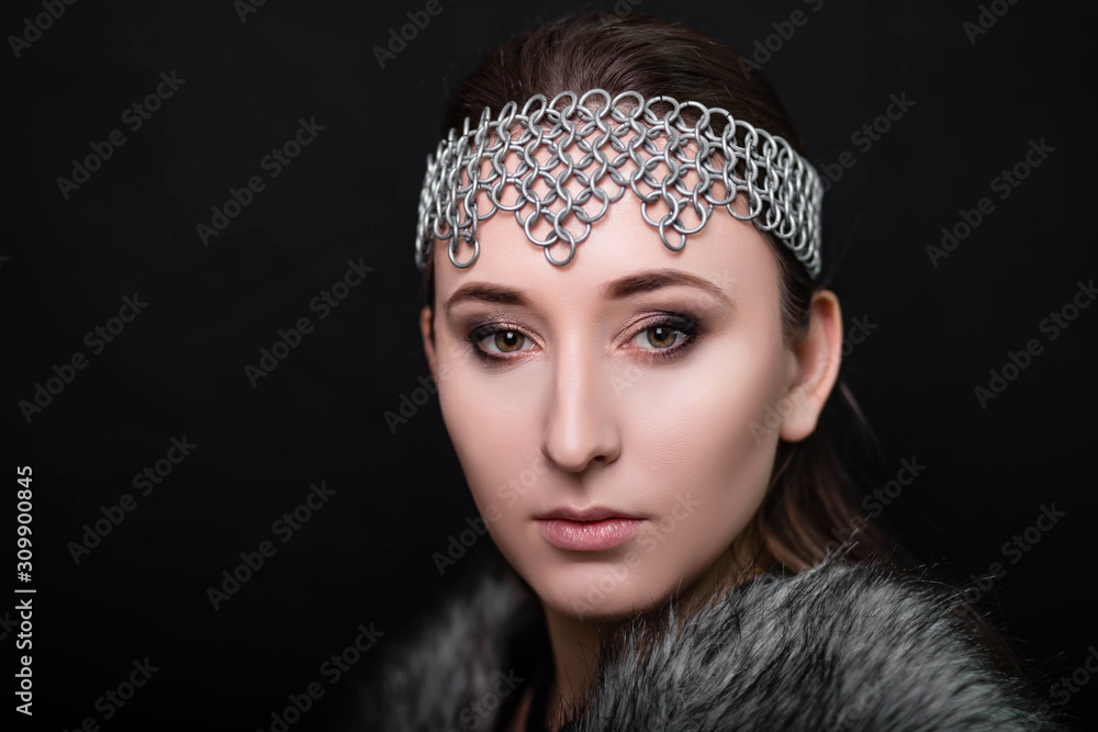 beauty portrait of a girl with a chain mail strip on her head and fur on her shoulders. Studio photo on a black background. Model with clear skin.