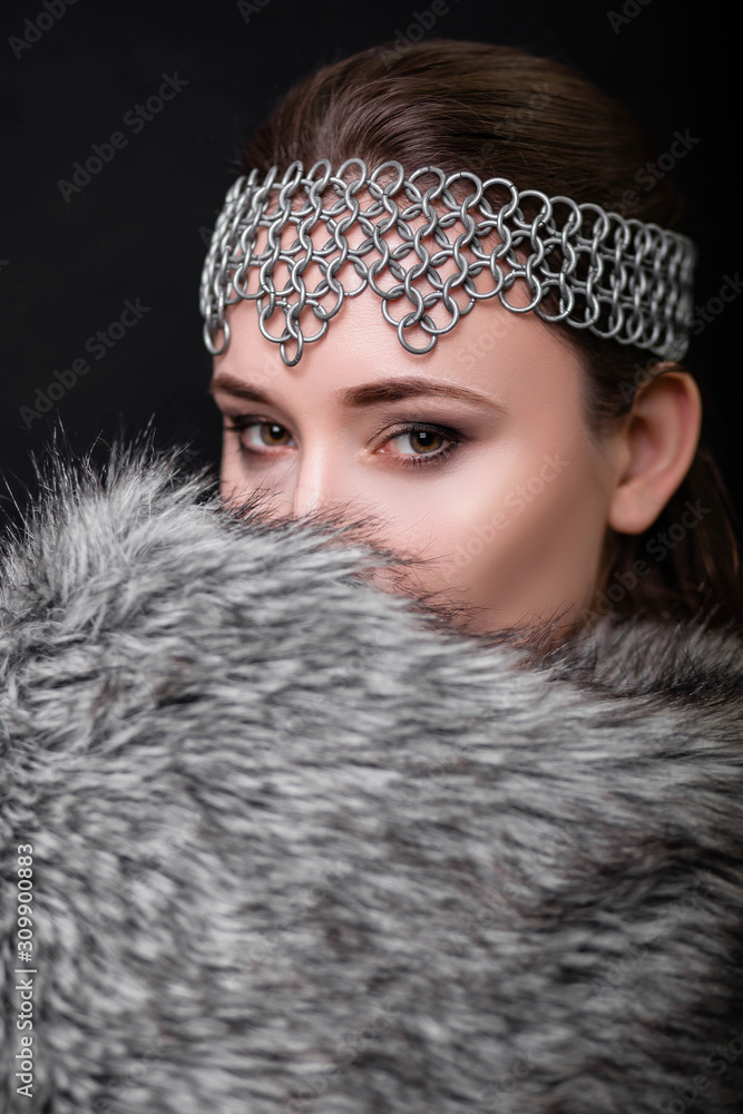 beauty portrait of a girl with a chain mail strip on her head and fur on her shoulders. Studio photo on a black background. Model with clear skin. beauty portrait of a girl with a chain mail strip on her head and fur on her shoulders. Studio photo on a black background. Model with clear skin.