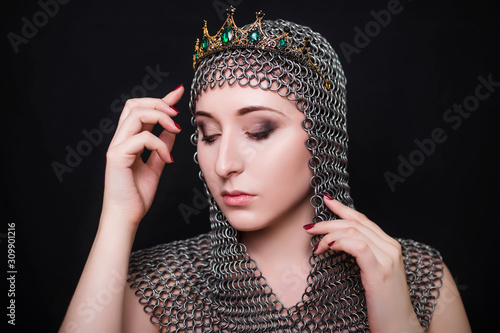 Beauty portrait of a girl in a chainmail hood with a crown on her head. Model with clear skin. Photo in studio on a black background.