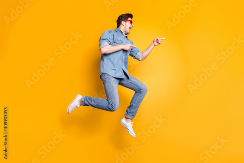 Full length body size view of nice attractive funky crazy cheerful cheery guy jumping pointing aside advert hot tour trip isolated over bright vivid shine vibrant yellow color background