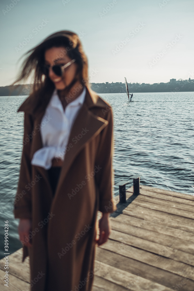 Beautiful Young Stylish Girl in Coat Walking in the Spring Beach at Sunset