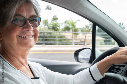 A senior people driving a car. The attractive senior woman looks at camera while driving and smiles © luciano
