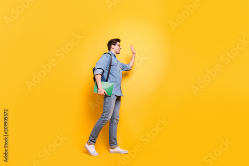 Full length body size profile side view of his he nice attractive cheerful cheery friendly guy walking waving meeting buddy isolated over bright vivid shine vibrant yellow color background
