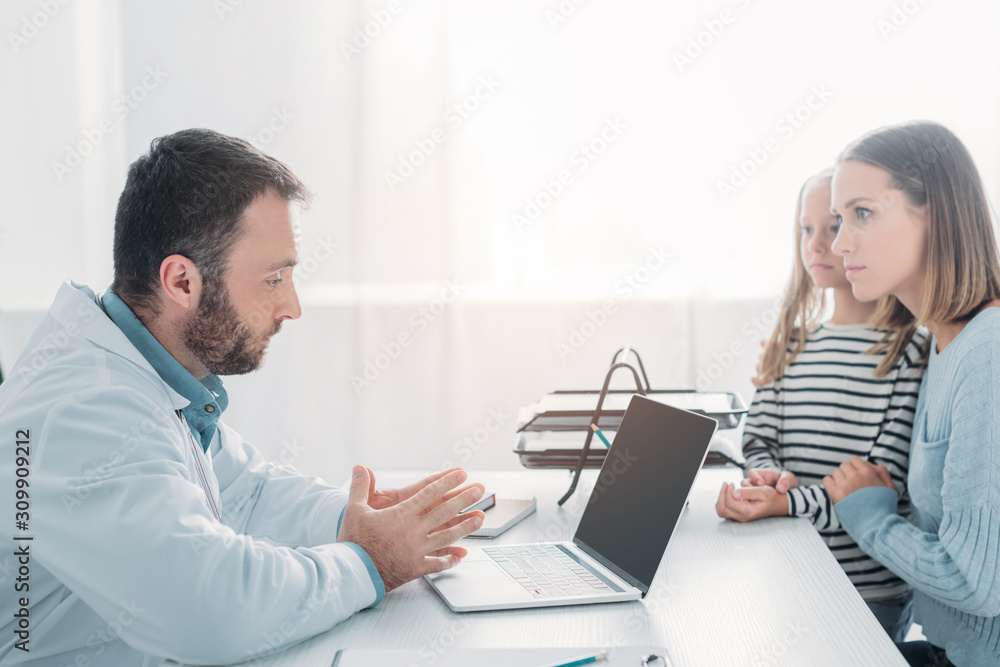 serious doctor talking to mother and daughter while sitting at table serious doctor talking to mother and daughter while sitting at table