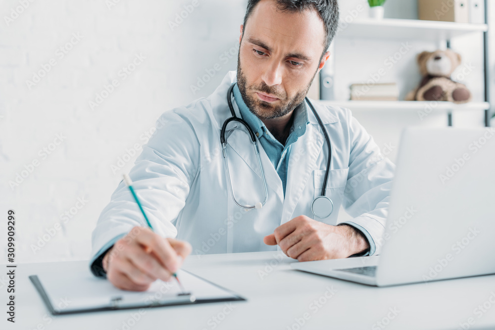 selective focus of attentive doctor writing prescription on clipboard selective focus of attentive doctor writing prescription on clipboard